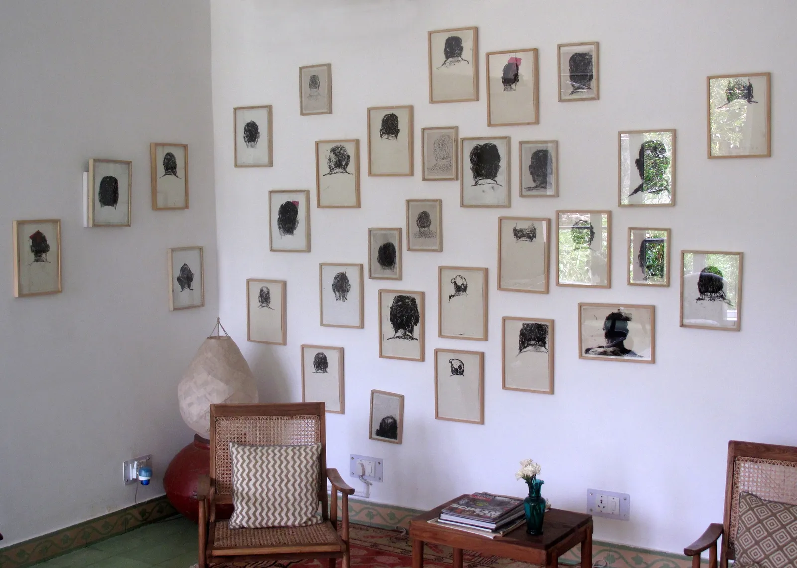 How Many Times? — installation of framed charcoal heads across a corner wall, Goa