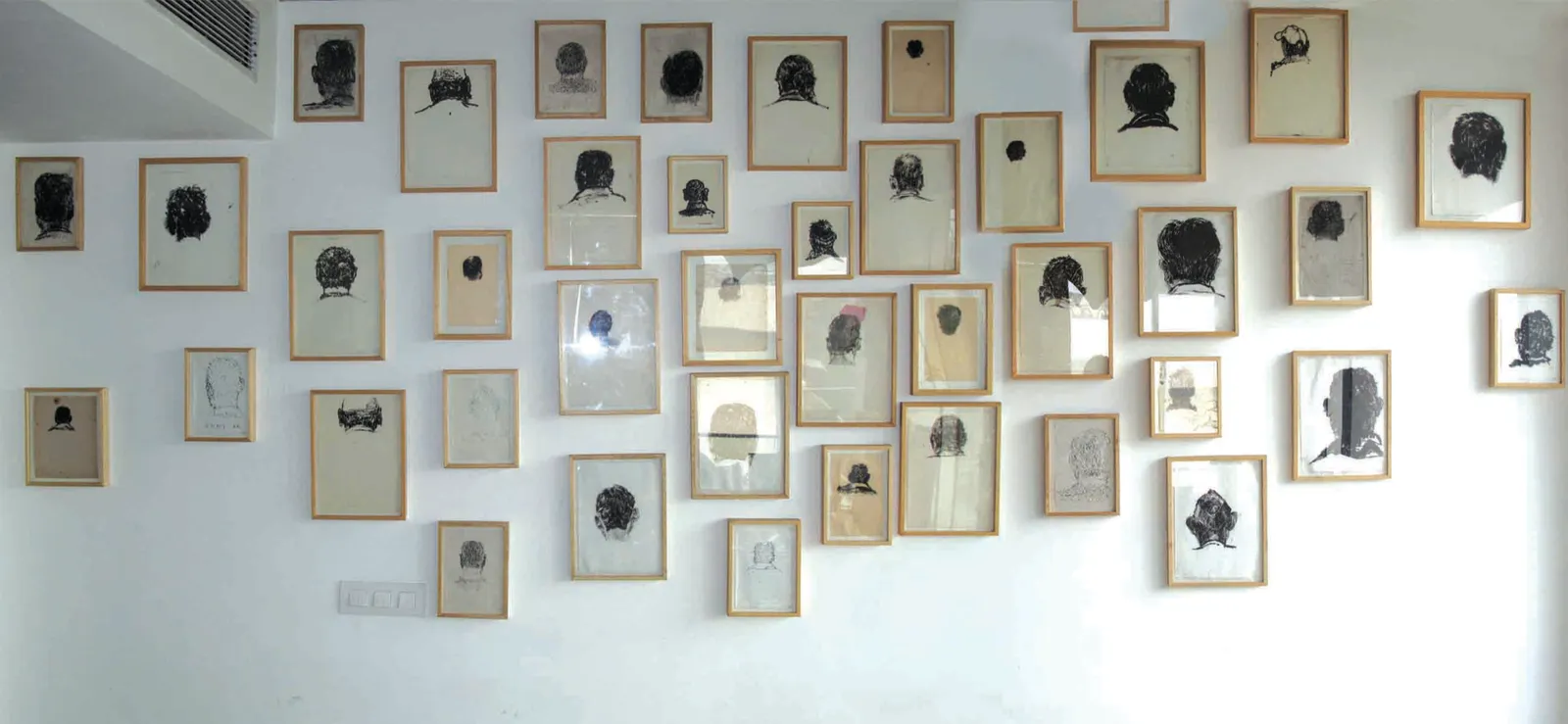 How Many Times? — installation of framed charcoal heads, dense grid formation