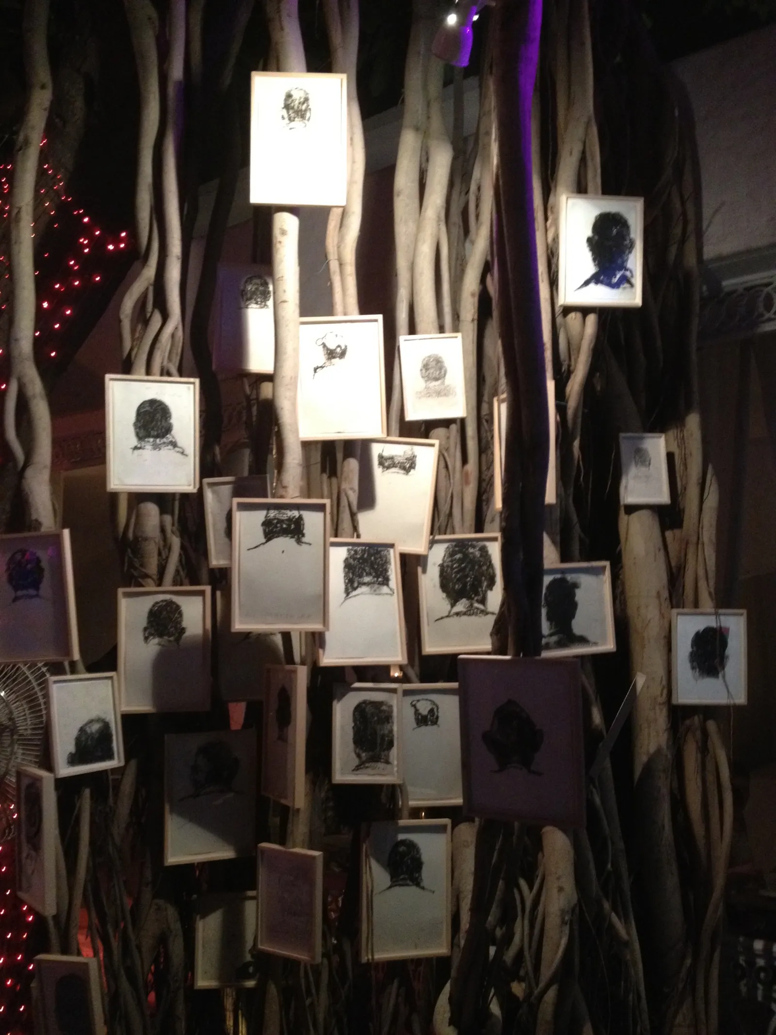 How Many Times? — framed charcoal heads hung in a banyan at night